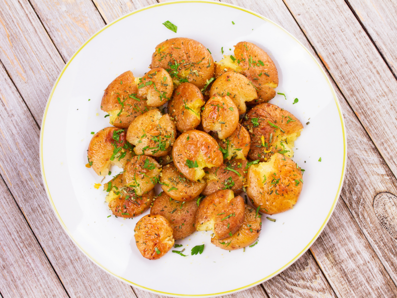 A plate of smashed potatoes with herbs and lemon zest.