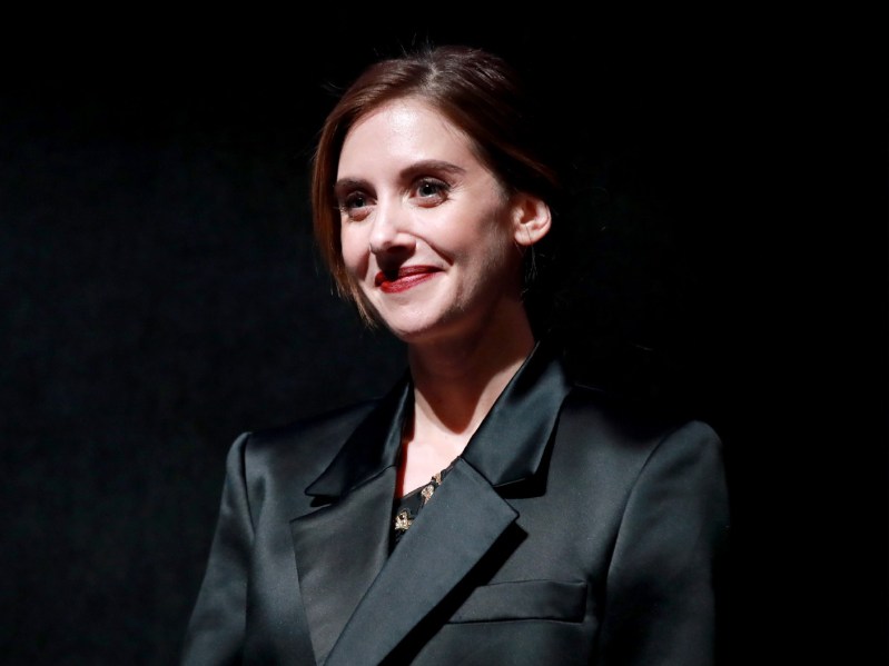Alison Brie wears a black suit jacket while onstage