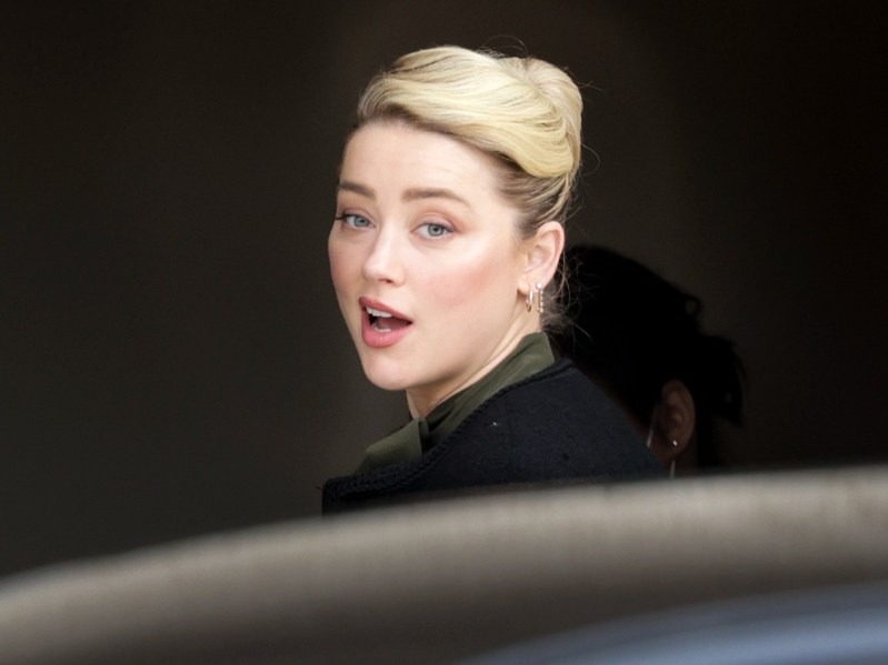 Amber Heard wears a dark coat and looks over her shoulder at photographers during her defamation trial with ex-husband Johnny Depp