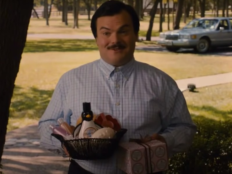 Jack Black smiles while holding a basket full of self-care items: lotion, nail files