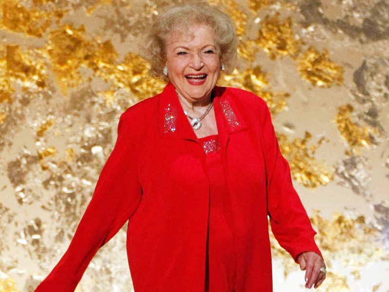 Betty White smiles while wearing a bright red pantssuit
