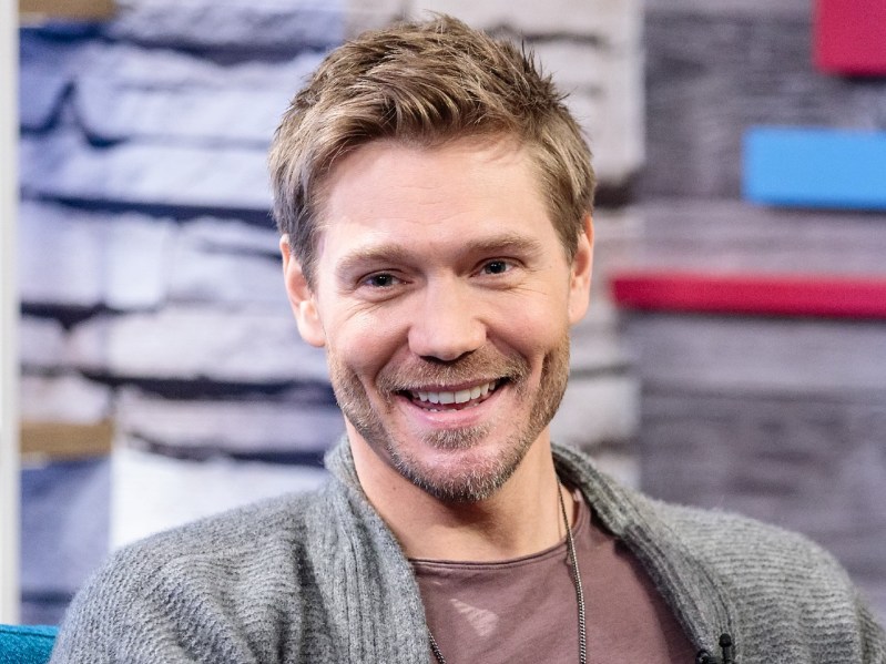 Chad Michael Murray smiling wearing mauve shirt with gray jacket and chain necklace