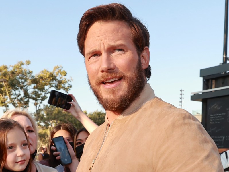 Chris Pratt standing outside and looking off into the distance. He is wearing a tan top