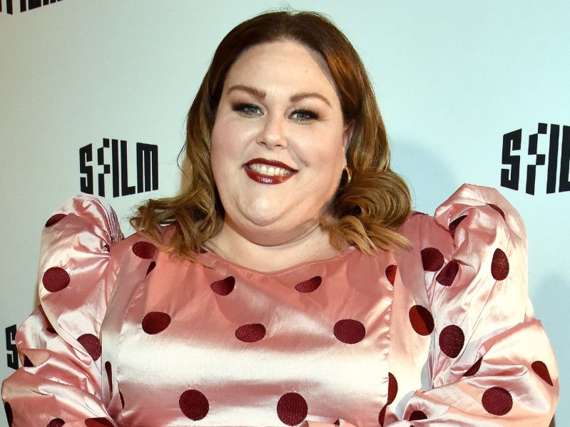 Chrissy Mets wearing pink satin dress with puffy sleeves and red polka-dots. She is wearing a deep red lipstick and has her shoulder-length hair in loose curls.
