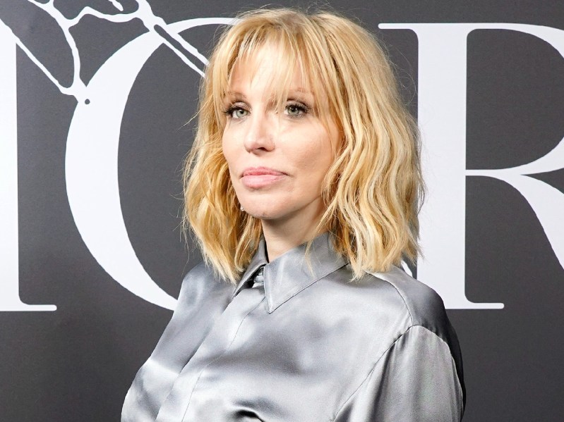 Courtney Love side-eyes the camera. She has on a silver mock-neck dress and her blonde hair is in a shag haircut
