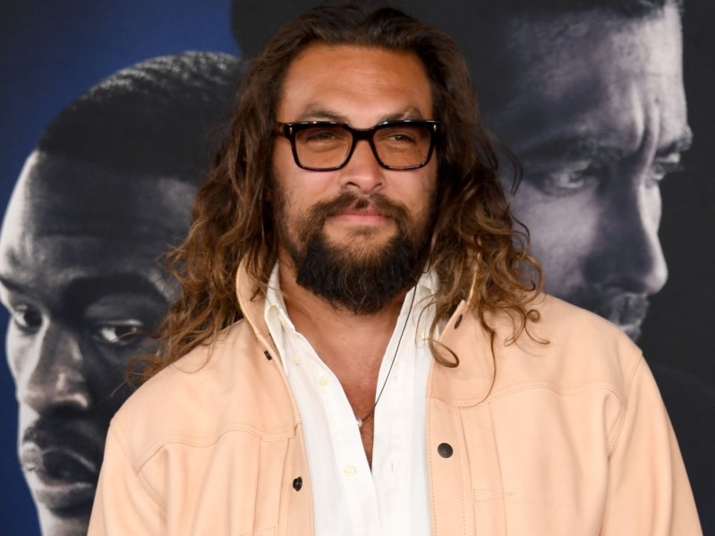 Closeup of Jason Momoa wearing black-rimmed glasses and a peach jacket over a white shirt