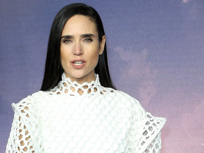 Jennifer Connelly wears a white dress against a blue and pink background on the red carpet