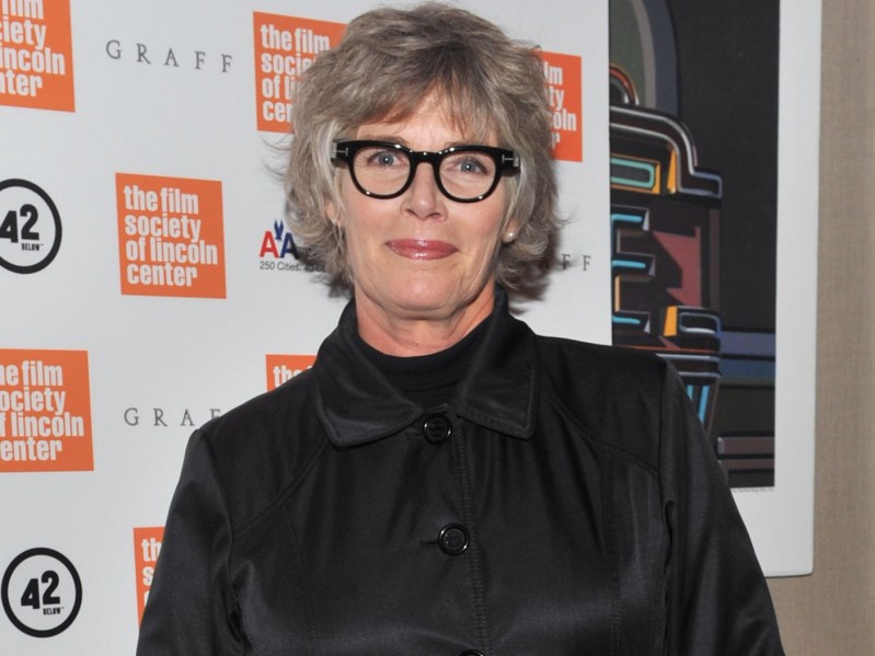 Kelly McGillis poses in black button-down top with thick-rimmed black glasses and red lipstick