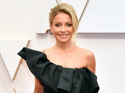 Kelly Ripa smiles while wearing a black off-shoulder gown