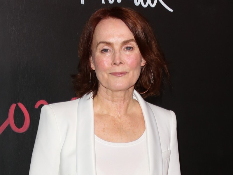 Laura Innes from the chest up, wearing all-white shirt and suit jacket combo. Her hair is cut slightly above the shoulders and is a deep red-brown