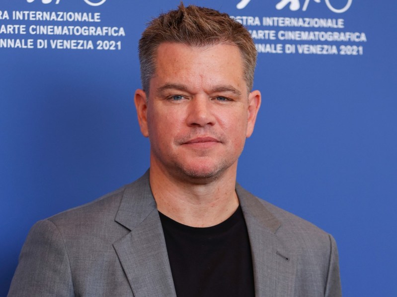 Matt Damon looks straight into the camera. He is wearing a black tee shirt under a gray blazer
