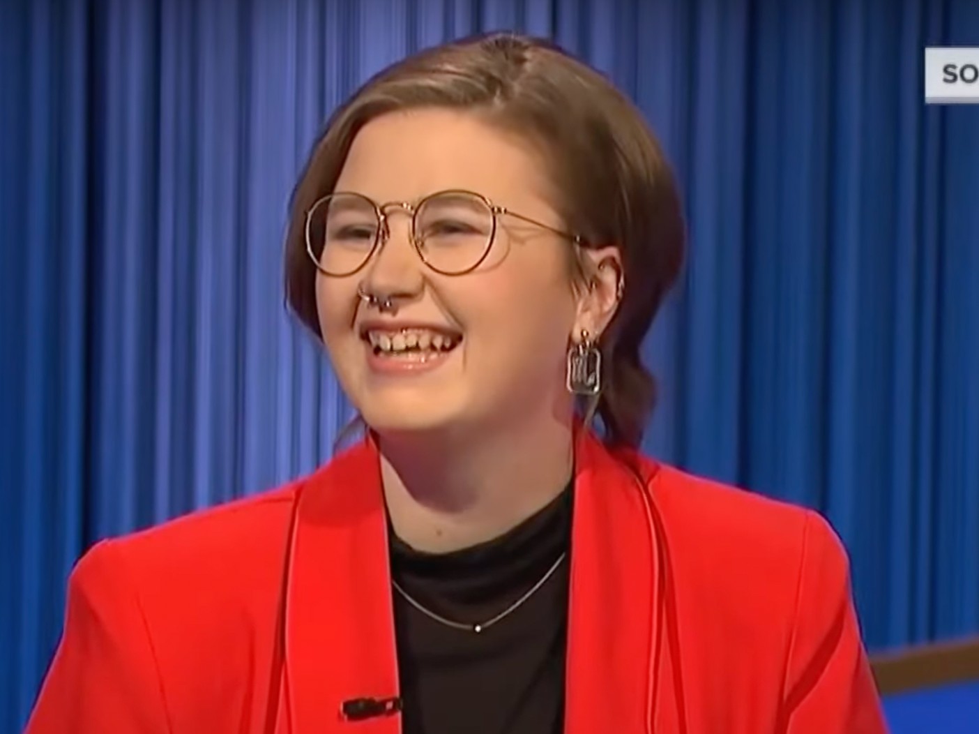 Mattea Roach laughs to someone off-camera. She is wearing a black top with a bright red-orange blazer