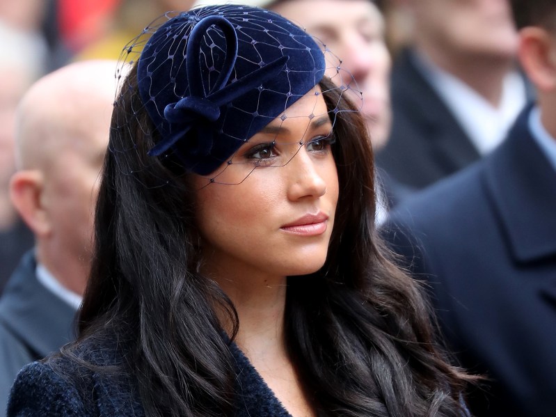 Meghan Markle looking serious in a black hat and small veil