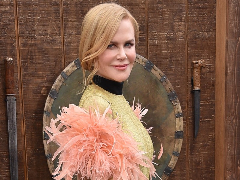 Nicole Kidman wears a feather-festooned dress on the red carpet in front of a wooden background