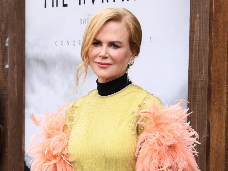 Nicole Kidman, with her hair in an updo, smiles while wearing a yellow-green dress with a thick black collar and peach feathers puffing out from the sleeves.