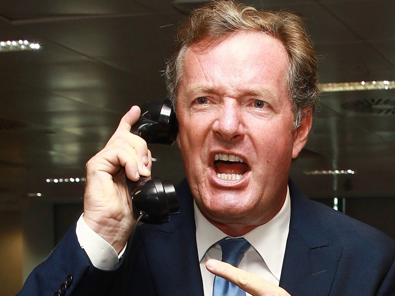 Closeup of Piers Morgan wearing suit and tie, yelling into phone receiver and pointing his finger