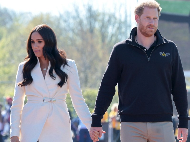 Meghan Markle, wearing a white coat, walks hand in hand with Prince Harry, in a dark jacket, at the Invictus Games 2022