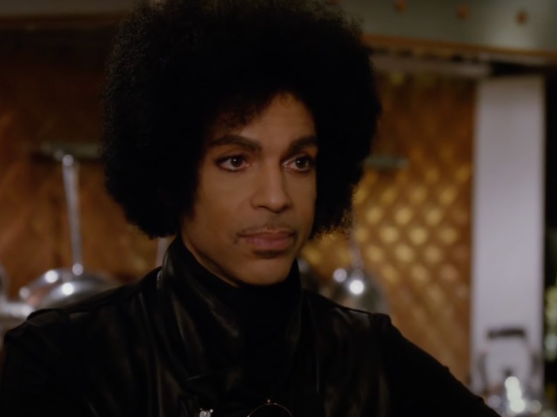 Prince looking off-camera, wearing all-black top with afro