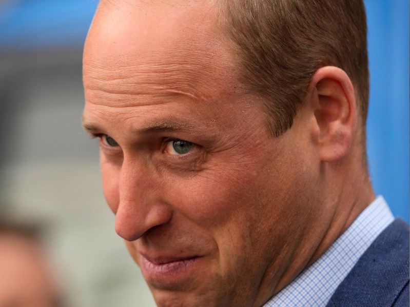 Prince William smiles over his shoulder while wearing a blue suit at a royal visit