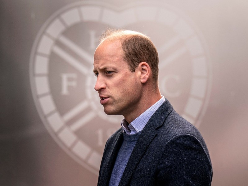 Prince William wears a dark suit against a silver-ish background