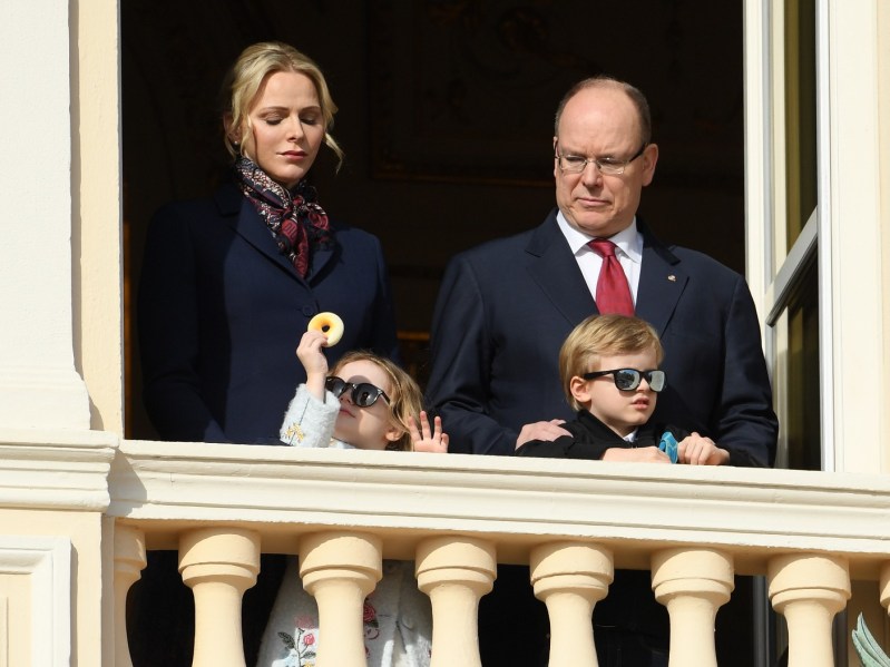 Princess Charlene (L) and Prince Albert (R) of Monaco overlook a balcony with their small children in front of them.
