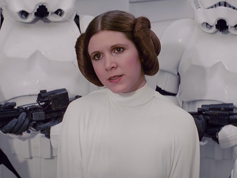 Carrie Fisher as Princess Leia, wearing white mock-neck smock and space buns, with a serious look on her face