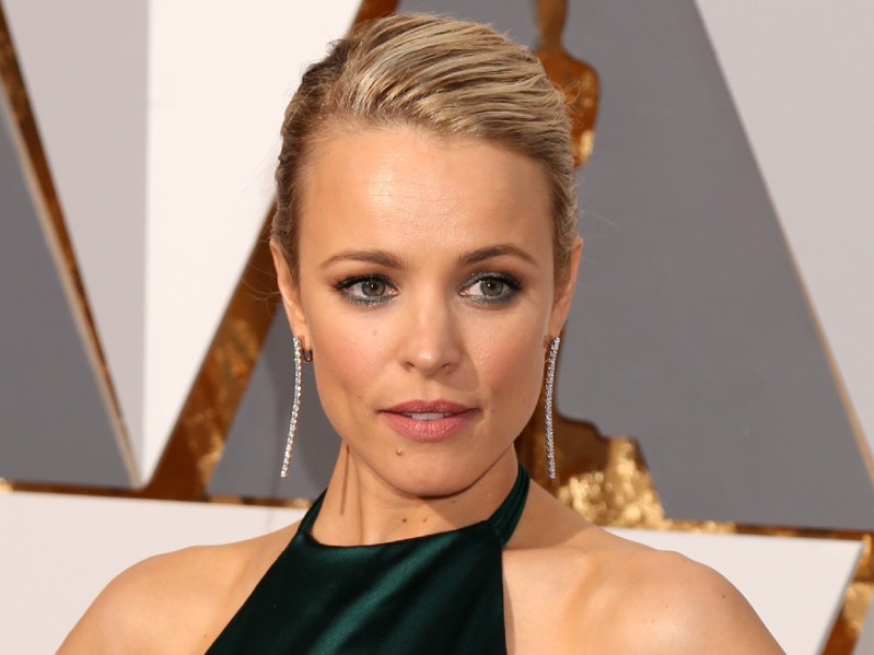 Rachel McAdams wears a green dress with her blonde hair pulled back in a bun on the Oscars red carpet