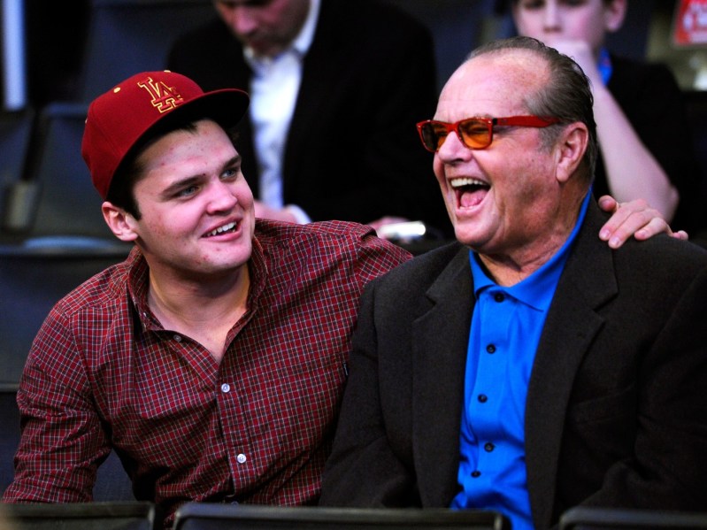 Ray Nicholson (L) wearing burgundy button-down and red baseball cap, with his arm around Jack Nicholson (R) wearing blue top and black jacket. The two are laughing and appear to be in conversation