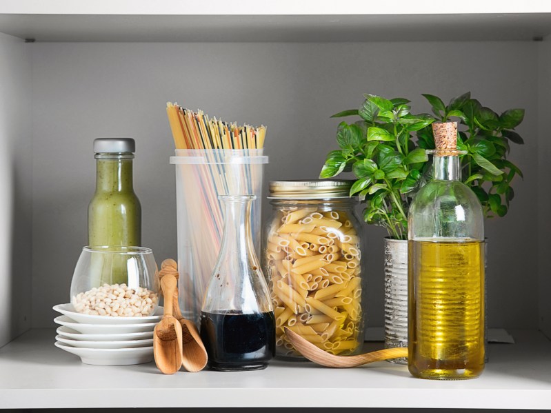 A clear bottle of olive oil being stored with dishes and other pantry staples.