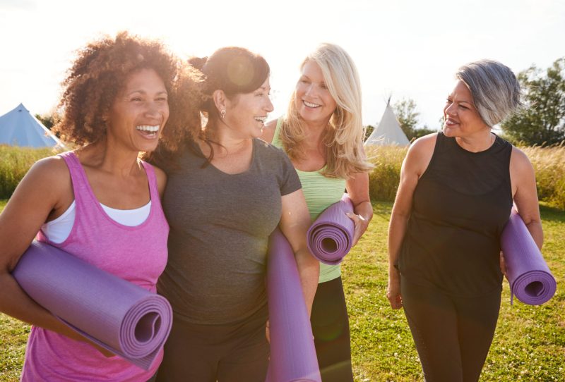 Group of female friends smiling and carrying yoga mats at a park