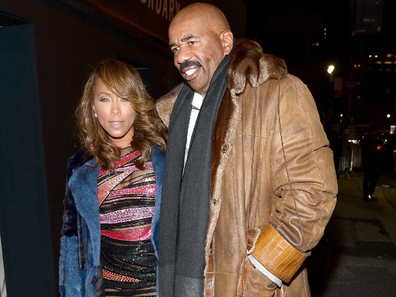 Marjorie Harvey, in a colorful dress and blue coat, stands with Steve Harvey, in a brown jacket, on a New York City street