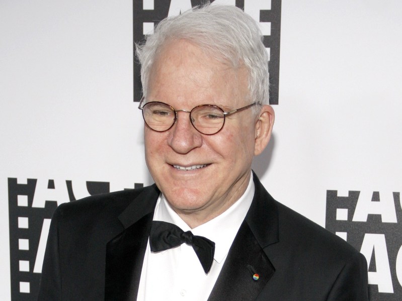 Steve Martin smiling wearing glasses and a white shirt with black suit jacket and black bow tie
