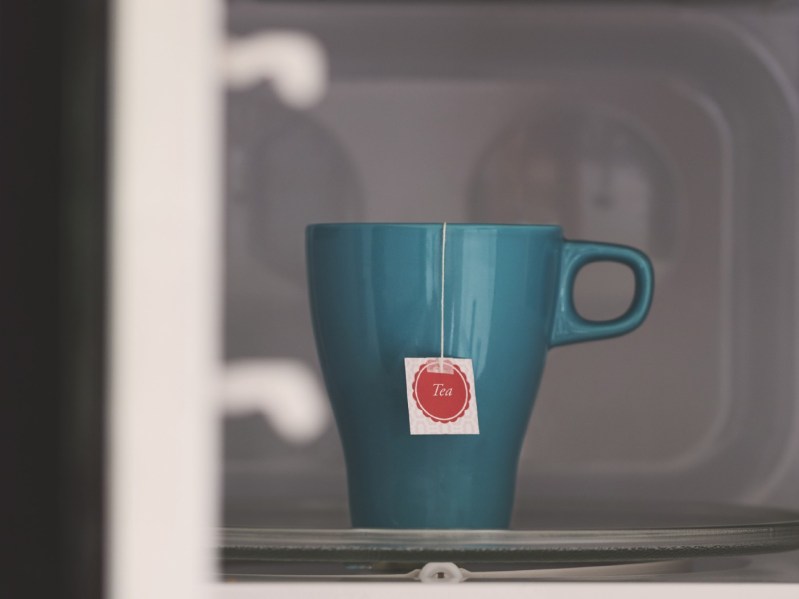Teal mug with a bag of tea in a microwave