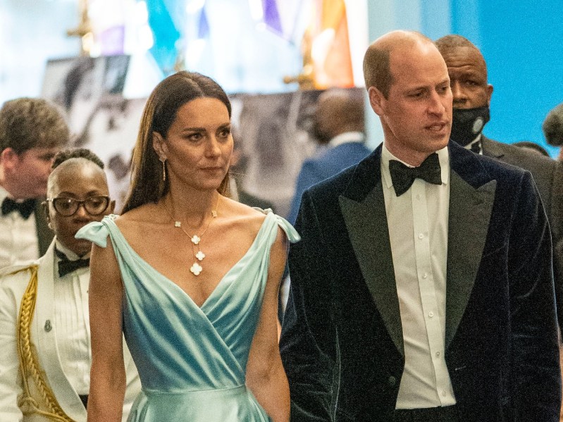 Kate Middleton (L) wearing sea-green gown and jewel necklace, walking next to Prince William, who is wearing a white shirt, black suit jacket, and black bow tie. Both are looking off to the right