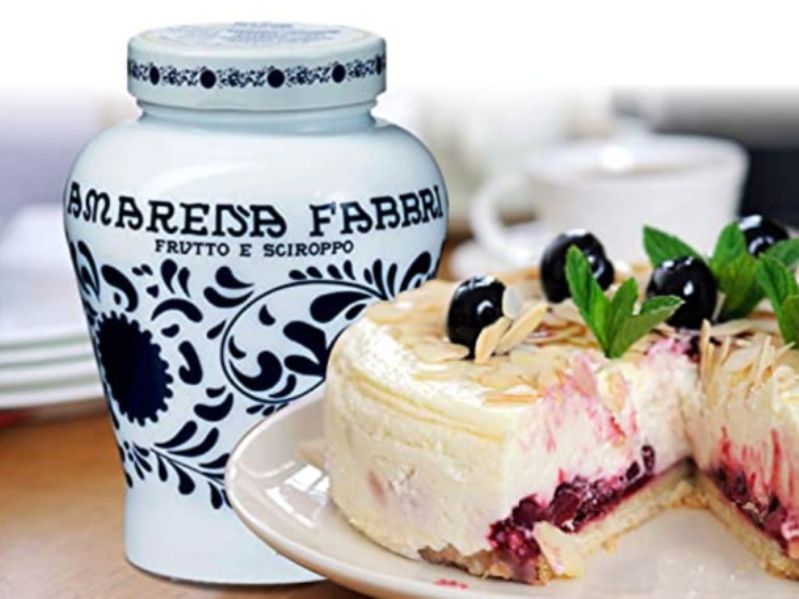 A blue and white jar Fabbri Amarena Wild Cherries sits by a cherry cheesecake