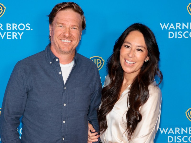 Chip Gaines (L) wearing blue button-down top, standing next to Joanna Gaines, who is wearing a white long-sleeved top