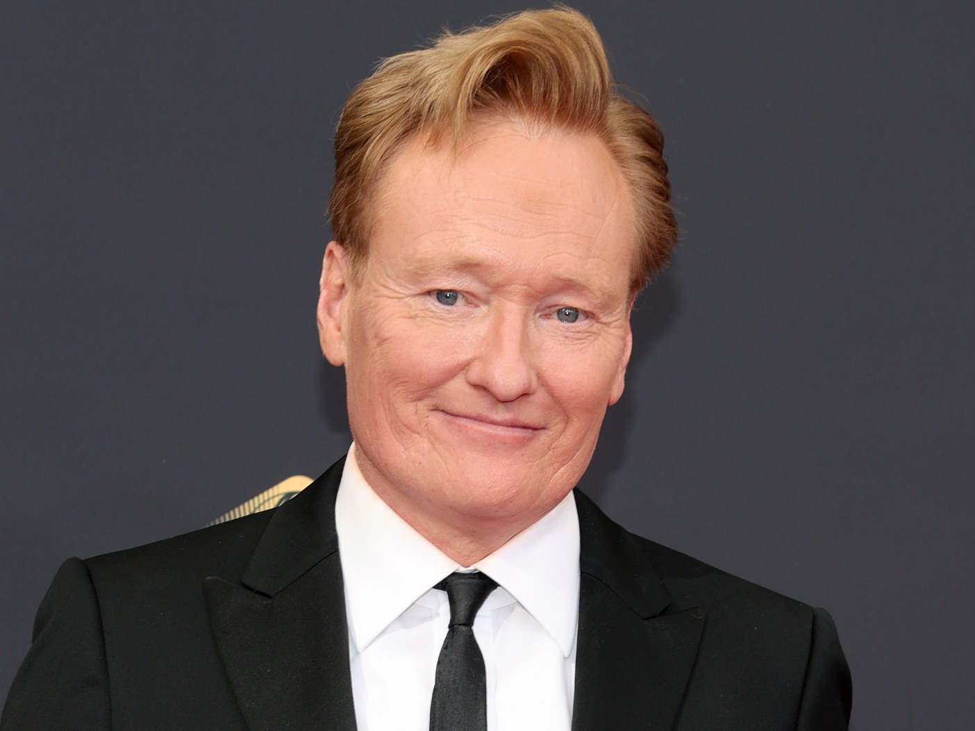 Conan O'Brien smiling in white dress shirt with black suit and tie