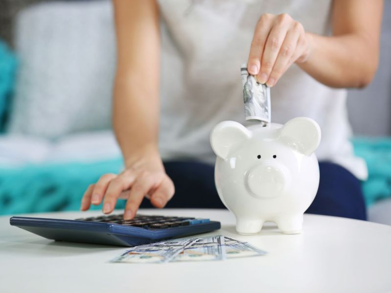 Female hand putting money into piggy bank and counting on calculator