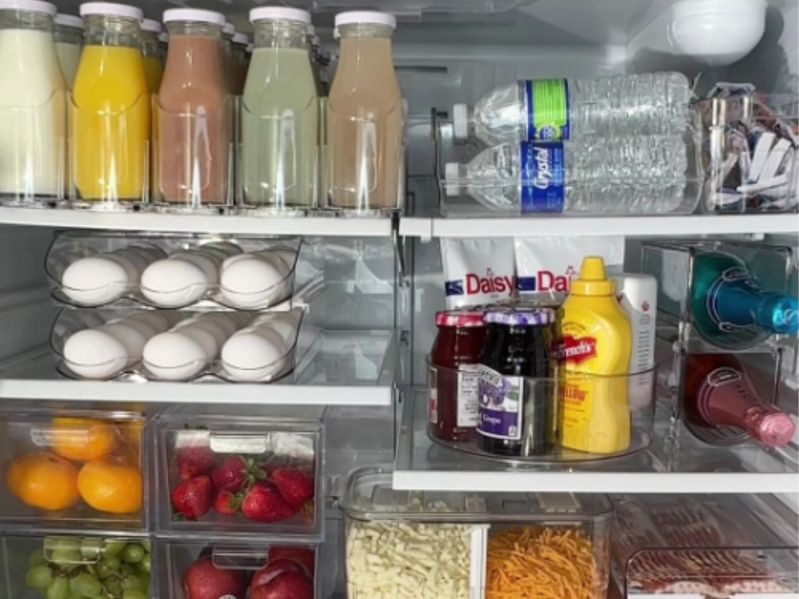 The inside of an organized refrigerator, with glass bottles, egg holder, lazy Susan, food saver containers