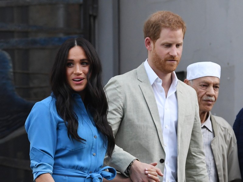 Meghan Markle (L) wearing blue smock dress and Prince Harry (R) wearing cream-colored blazer