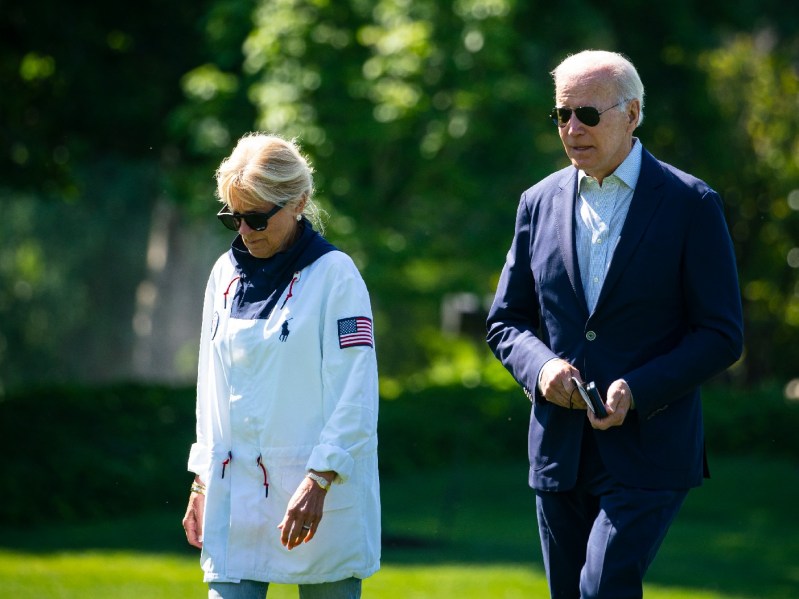 Jill Biden, in a white jacket, walks with husband President Joe Biden, in a dark suit, across the White House lawn