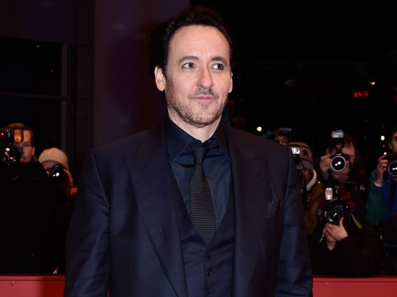 John Cusack wearing deep navy blue ensemble and looking off to one side