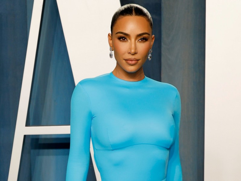 Kim Kardashian looks straight ahead. She is wearing a bright blue, long-sleeved gown and her hair is slicked back