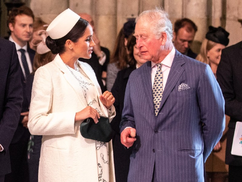 Meghan Markle (L) wearing white coat and pillbox hat, speaking to Prince Charles
