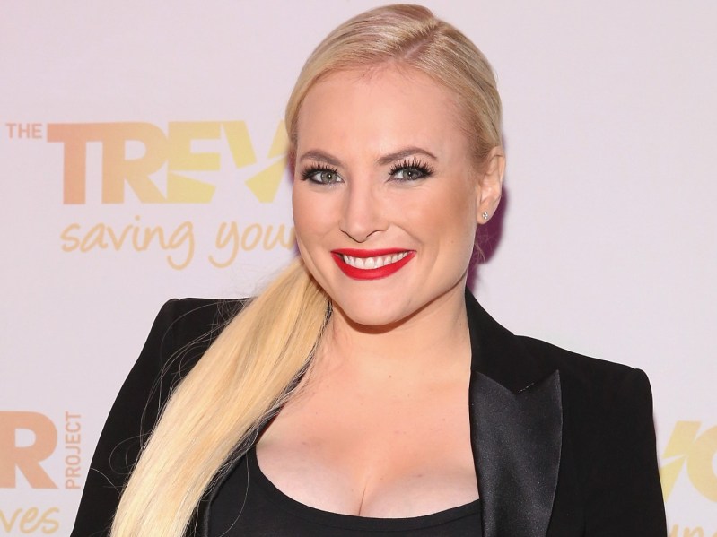 Meghan McCain smiles wearing red lipstick, a black outfit, and a long ponytail