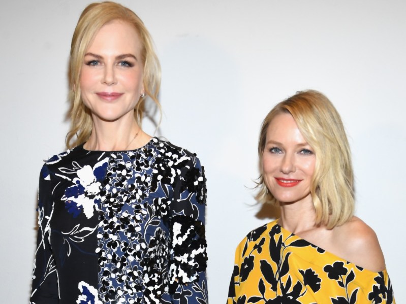 Nicole Kidman, wearing a black print dress, stands with Naomi Watts, in a yellow dress, against a white background