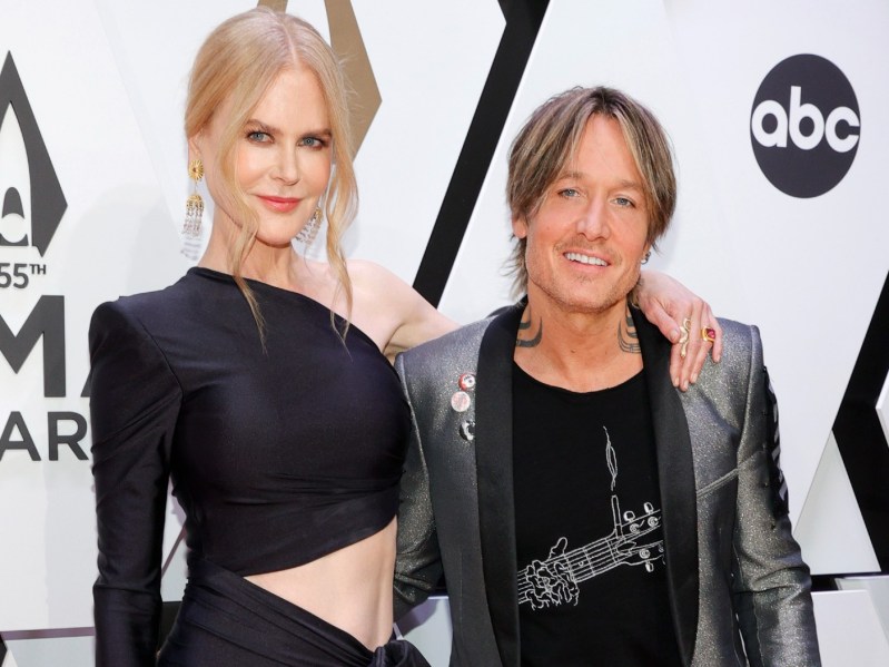 Nicole Kidman (L) wearing black cutout dress, standing next to Keith Urban who is wearing a black graphic tee with a silver blazer