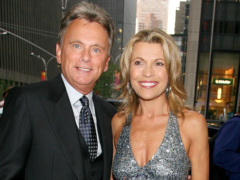 Pat Sajak (L) wearing black tuxedo and Vanna White wearing halter-top silver sequined dress