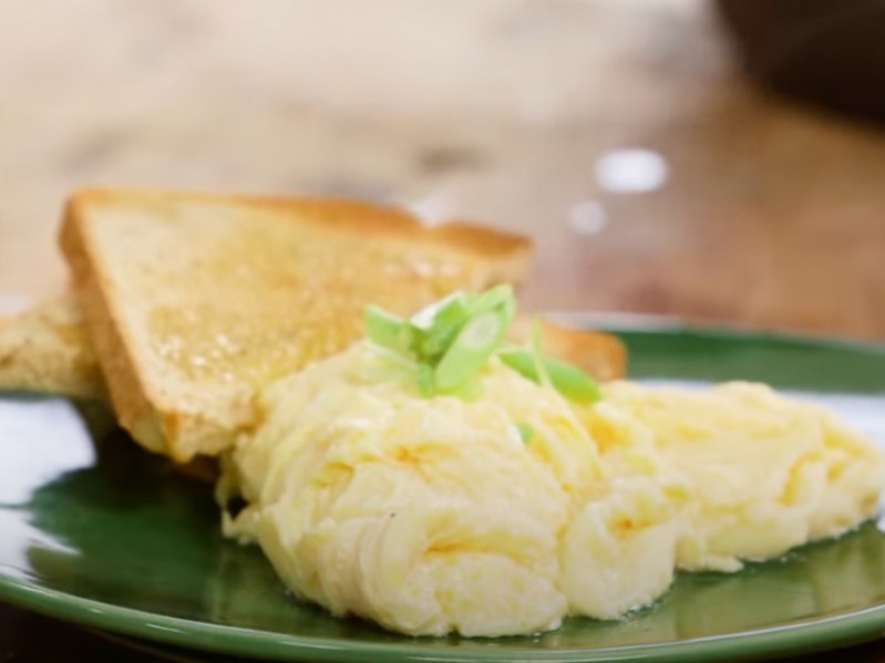 Green plate with poached scrambled eggs with green onion on top and toast in the background