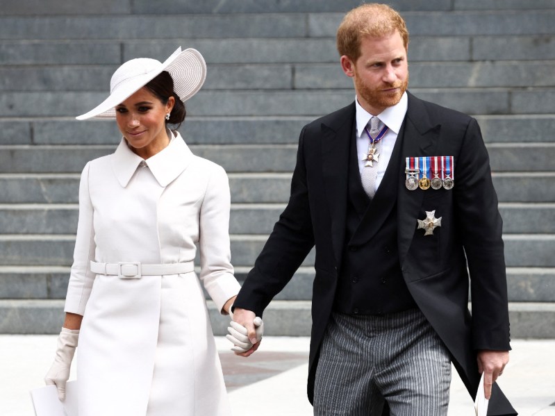 Meghan Markle, in a white coat and hat, walks with husband Prince Harry in a dark suit, down the stairs of St. Paul's Cathedral